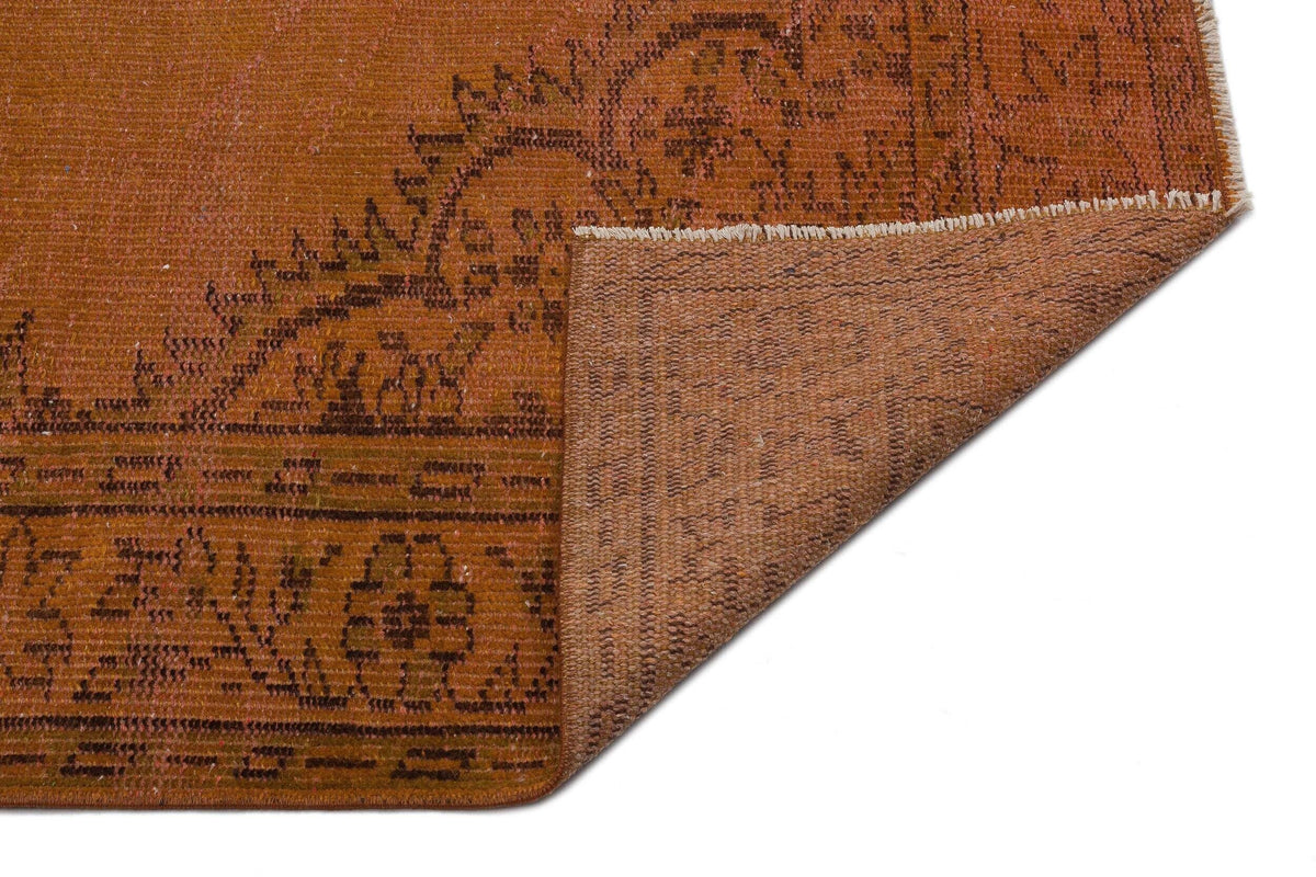 Rust-colored rug with a dark brown floral medallion pattern and a folded corner revealing the textured backing.