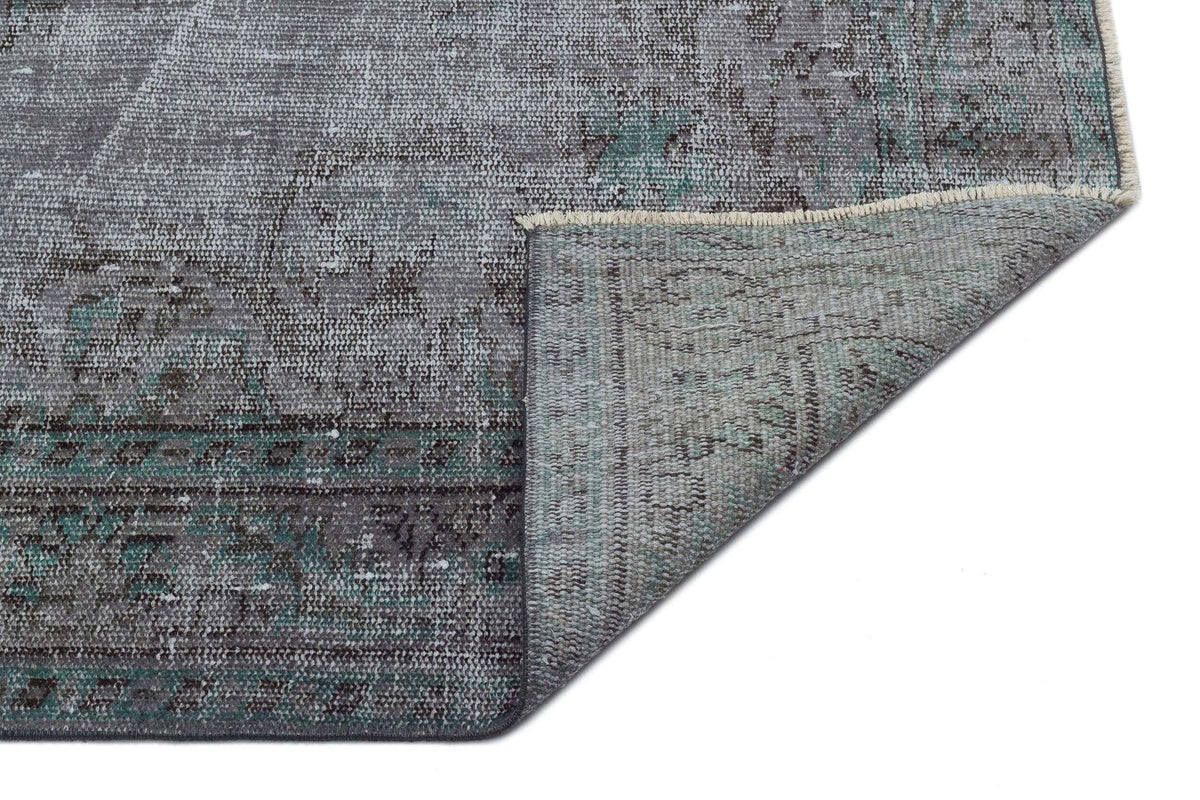 Distressed grey and teal vintage-style rug with a traditional medallion pattern, shown with a corner folded over.