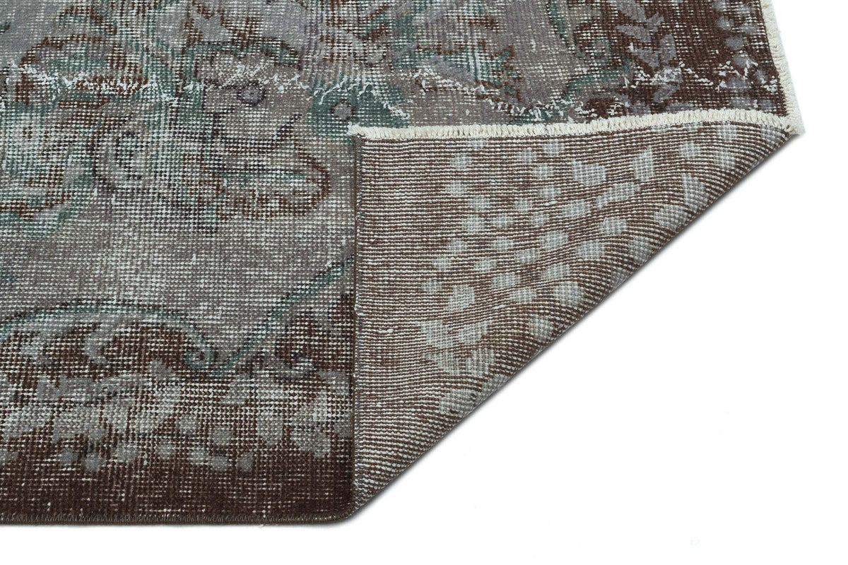 Distressed brown, grey, and teal medallion rug with a folded corner revealing the woven backing.