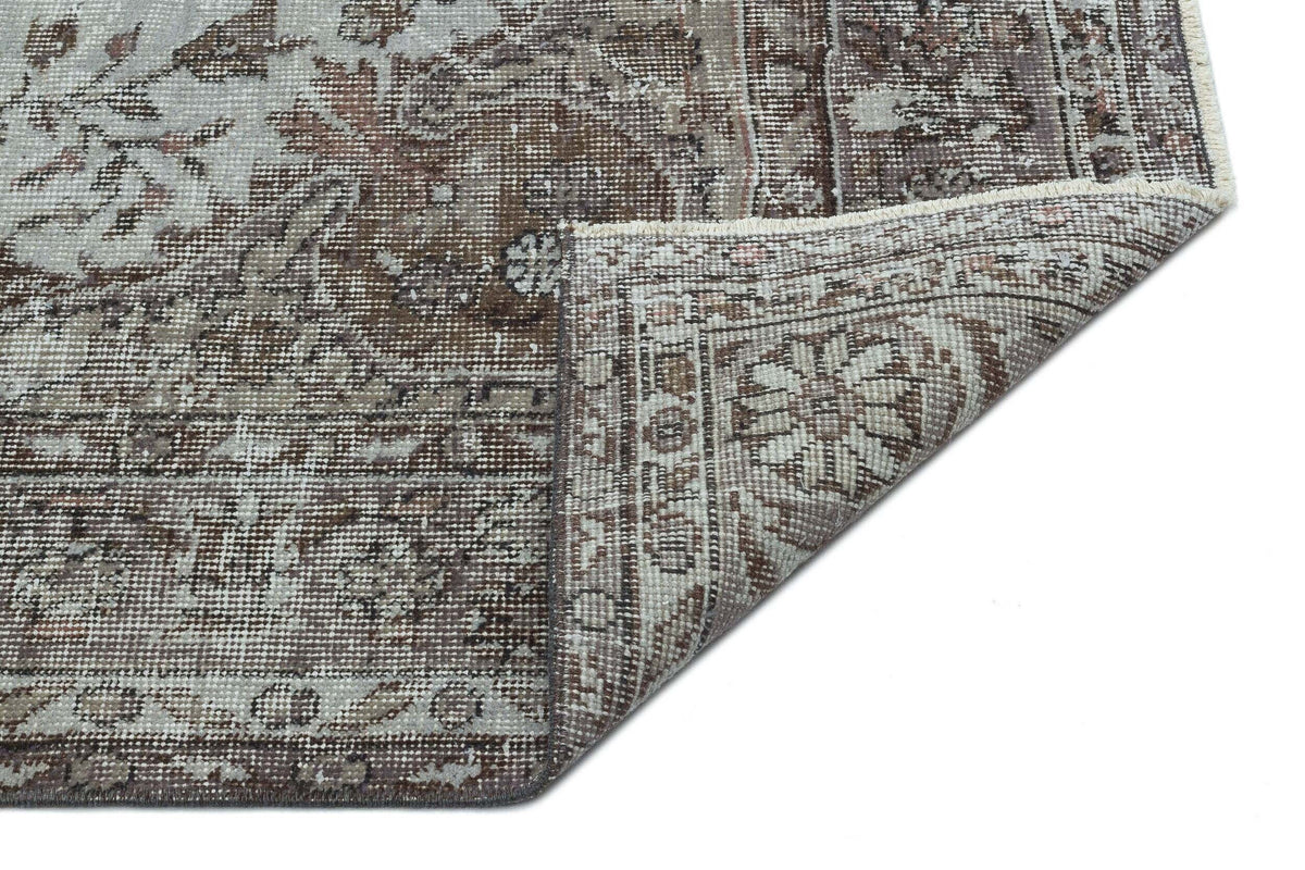 Brown and grey distressed traditional rug with a floral medallion pattern, shown with a corner folded over.