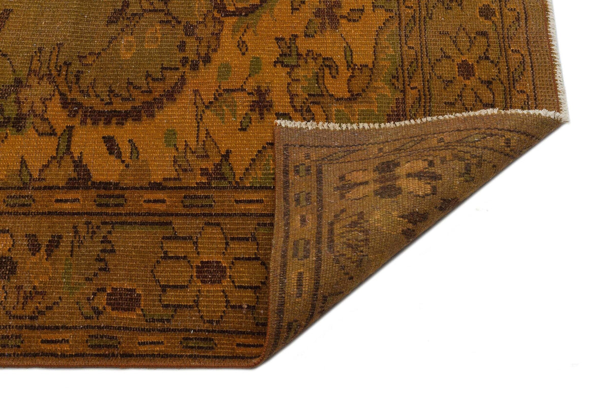 Mustard and brown traditional rug with a floral border and corner fold, isolated on a white background.