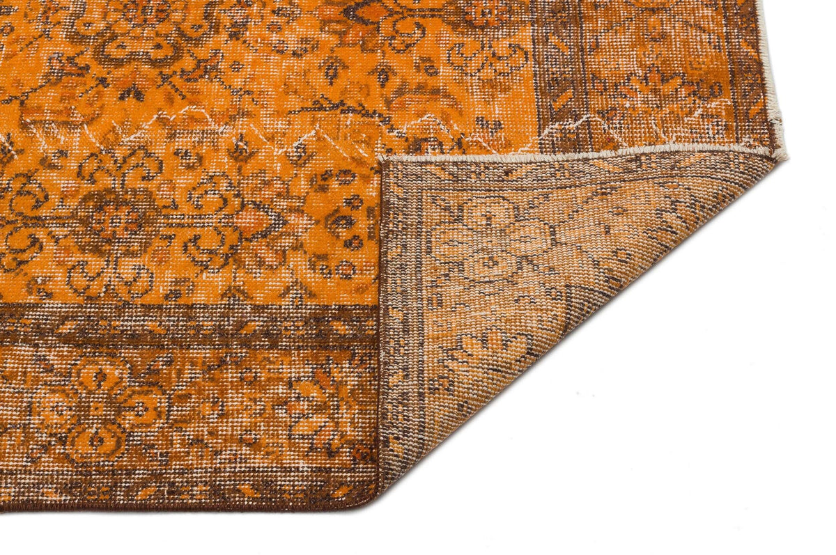 Distressed orange and brown rug with a traditional floral medallion pattern, shown with a corner folded over.