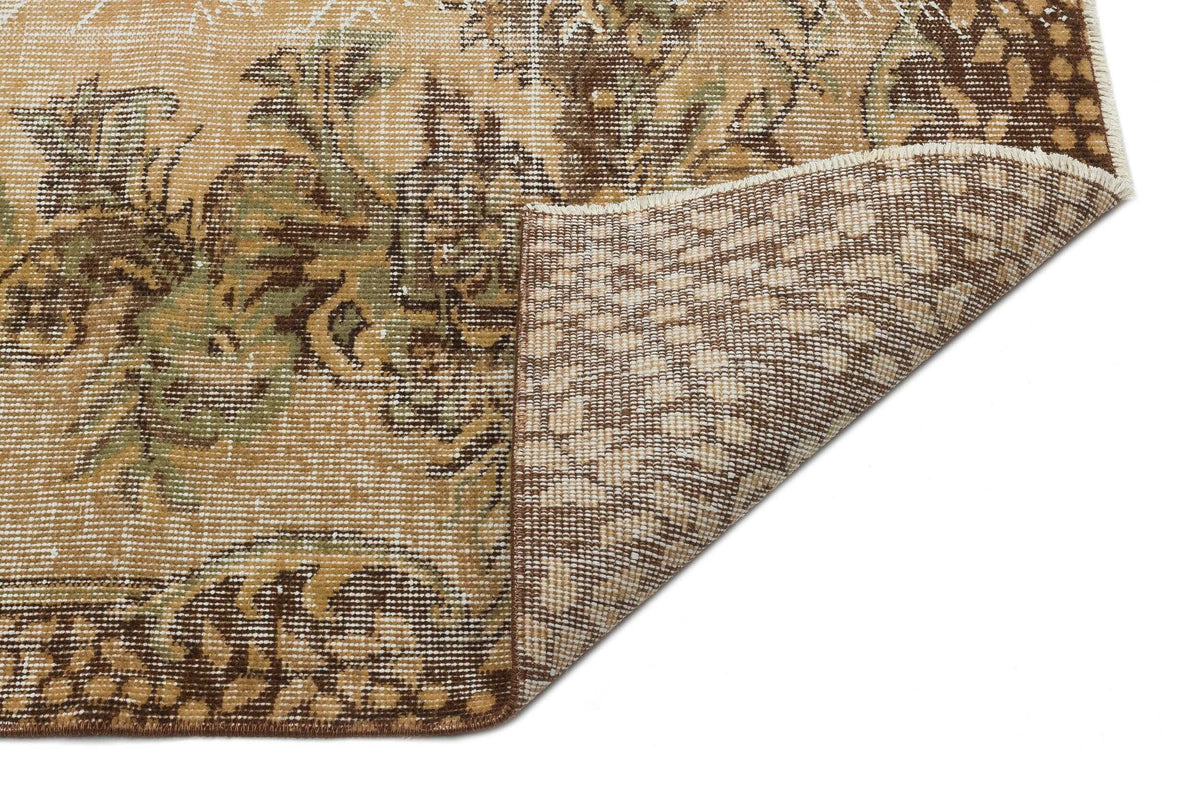 Tan and brown traditional rug with a distressed floral medallion pattern, showing a folded corner on a white background.