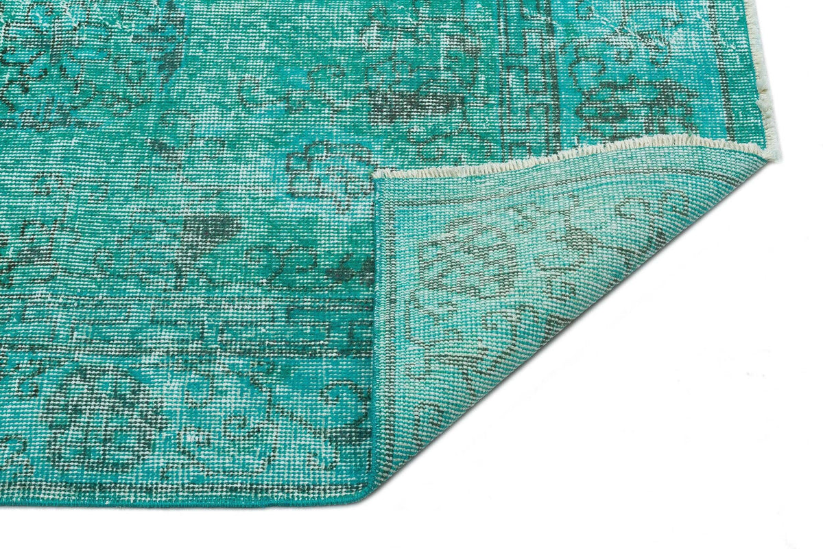Teal and dark grey distressed medallion pattern rug with a folded corner showing the woven backing.