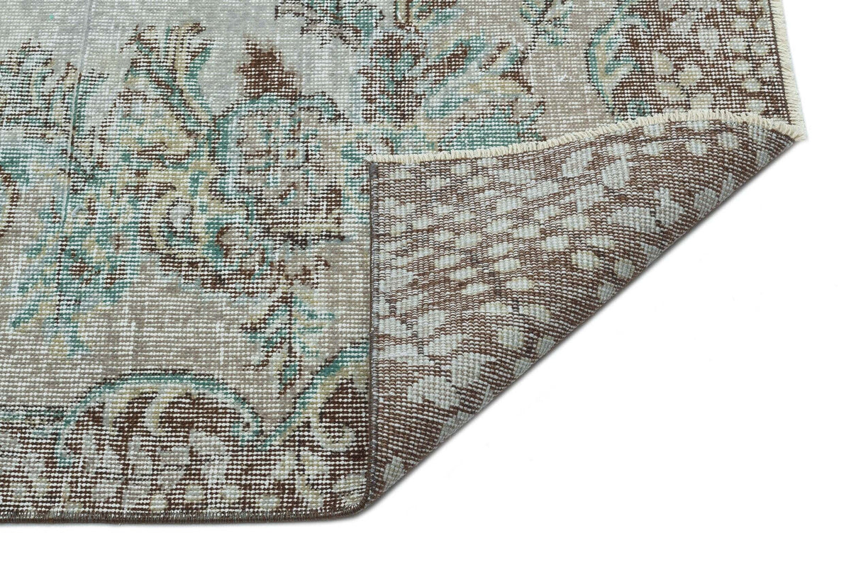 Distressed beige, brown, and teal floral medallion rug with a corner folded over to reveal the woven backing.