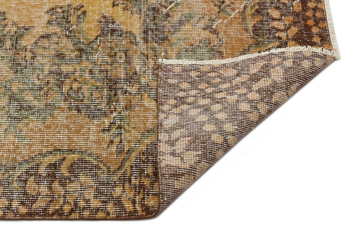 Ochre, brown, and green vintage-style rug with a floral medallion pattern, showing a folded corner on a white background.
