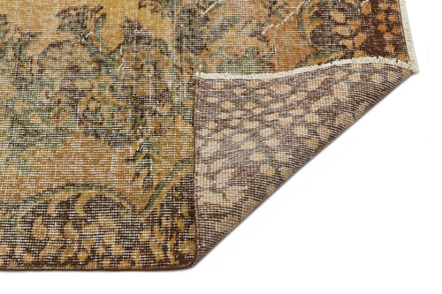 Load image 1 in gallery view. Ochre, brown, and green vintage-style rug with a floral medallion pattern, showing a folded corner on a white background.