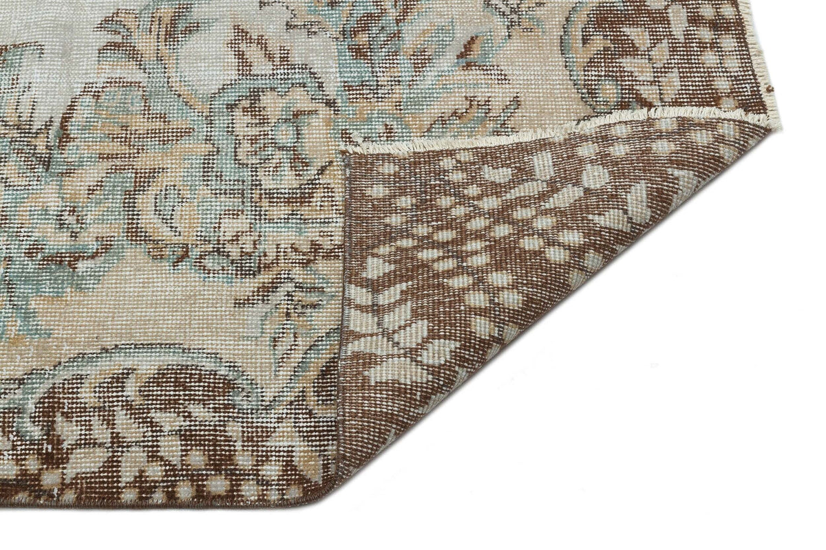 Beige, brown, and sage green vintage-style rug with a floral medallion pattern, shown with a corner folded over.