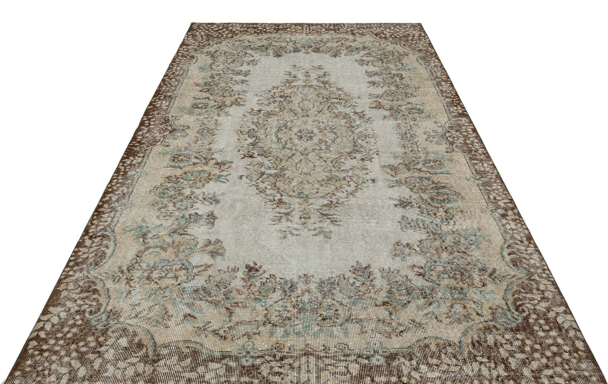 Distressed beige and brown traditional rug with a central floral medallion and ornate border on a white background.