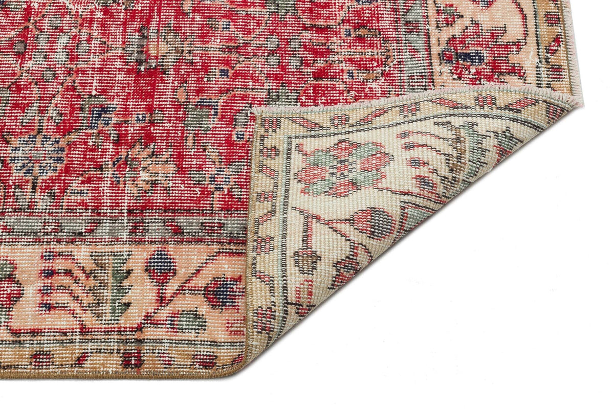 Red and beige traditional rug with a floral medallion pattern, shown with a corner folded over on a white background.