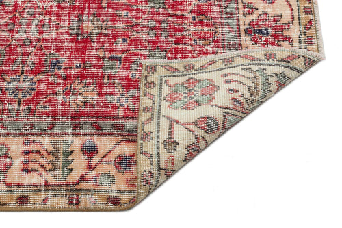 Load image 1 in gallery view. Red and beige traditional rug with a floral medallion pattern, shown with a corner folded over on a white background.