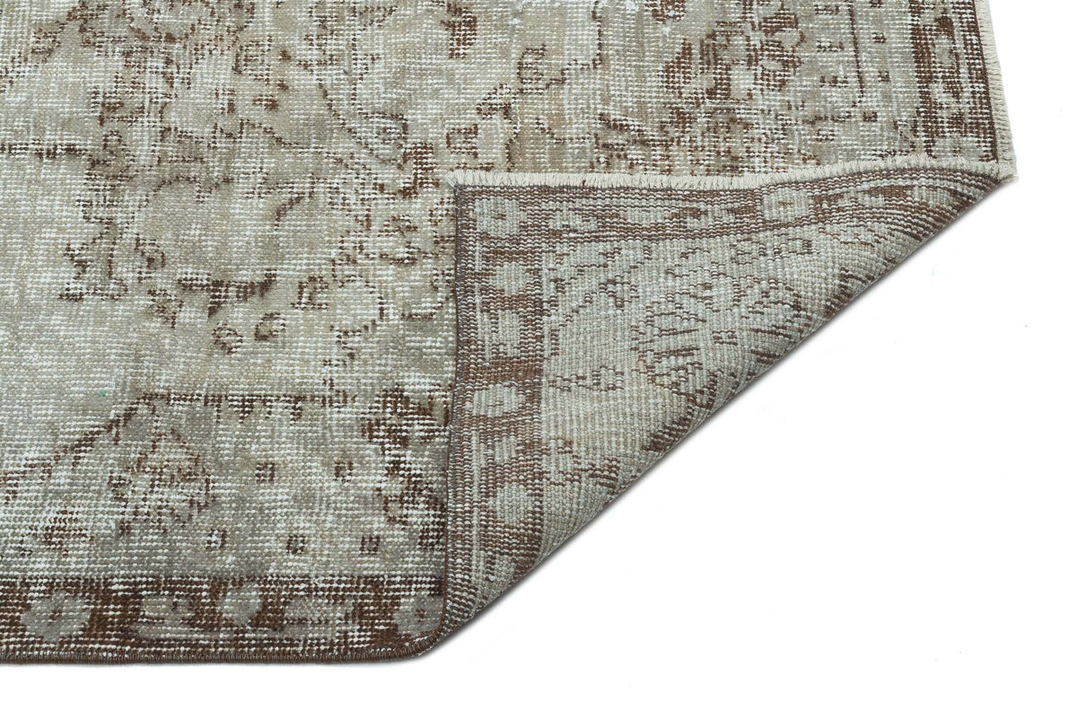 Beige and brown distressed traditional rug with a floral medallion pattern, shown with a corner folded over.