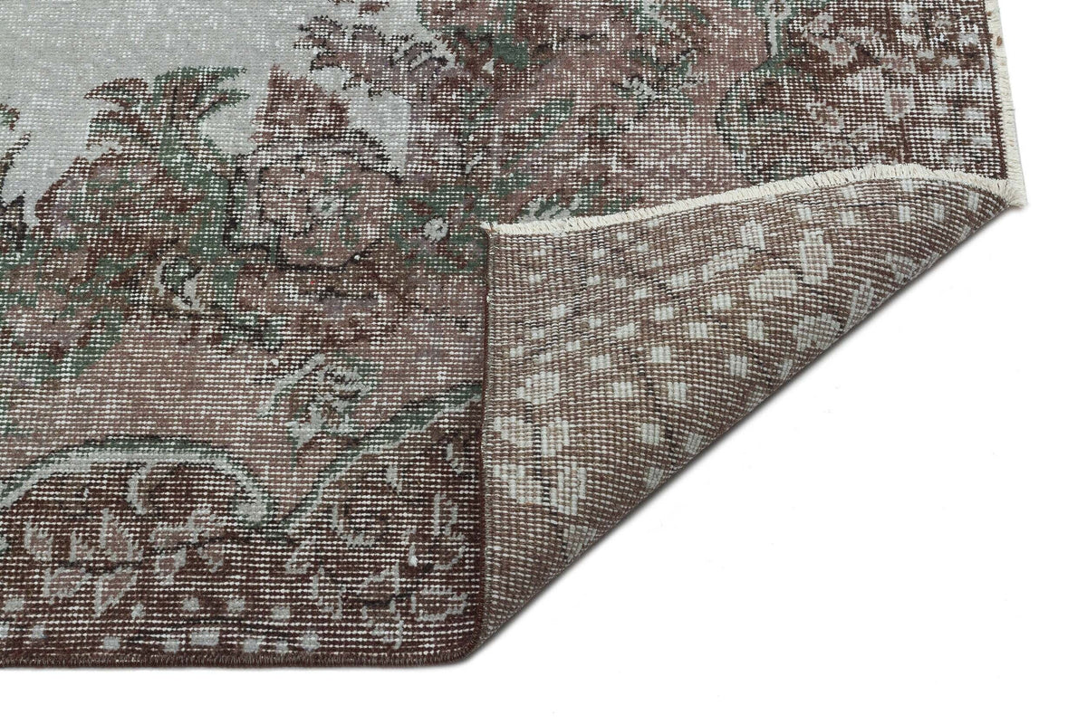 Distressed brown, sage green, and cream floral medallion rug with a folded corner showing the woven backing.