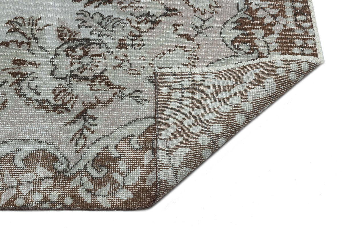 Distressed brown and beige rug with a traditional floral medallion pattern, shown with a folded corner on white.