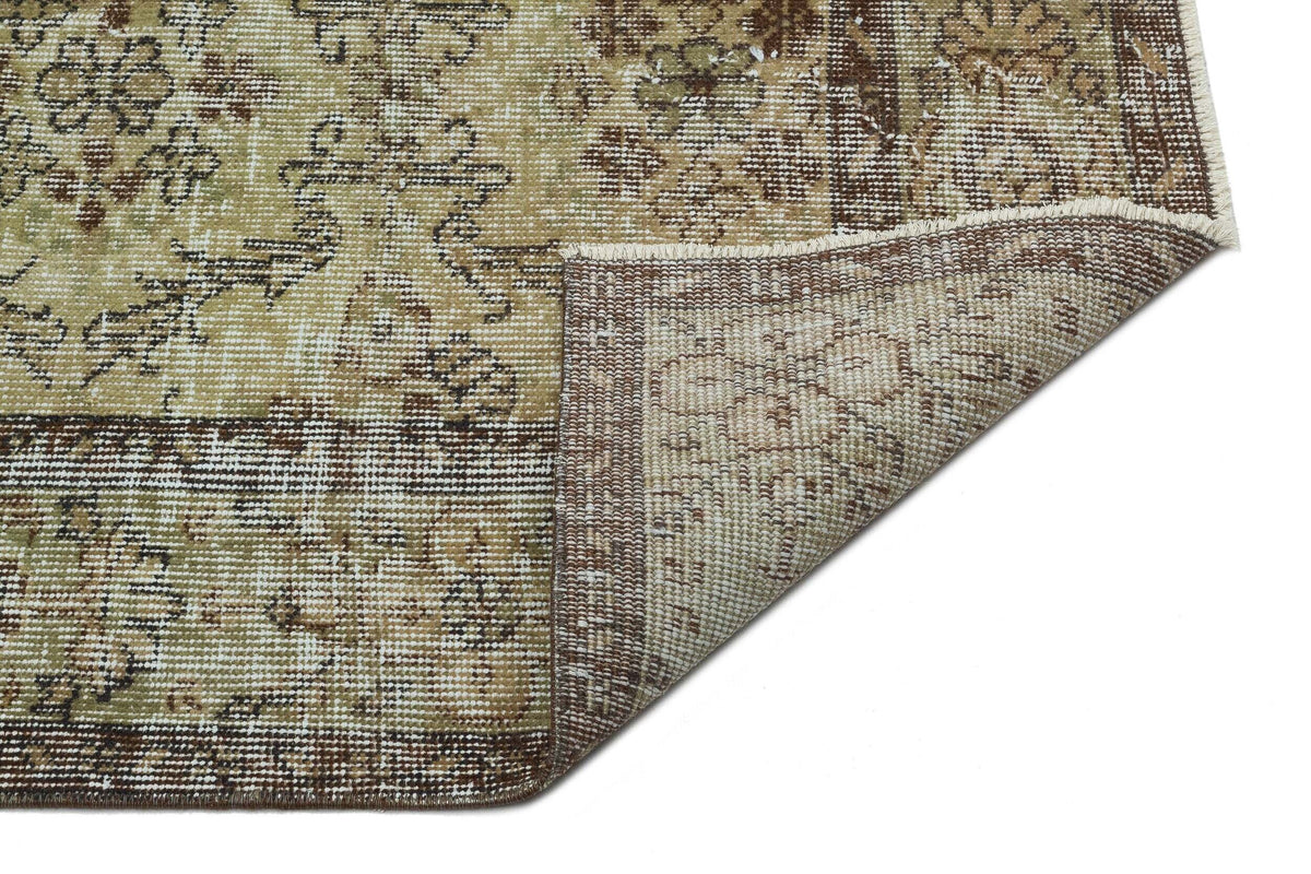 Distressed beige and brown rug with a traditional floral medallion pattern, shown with a corner folded over.