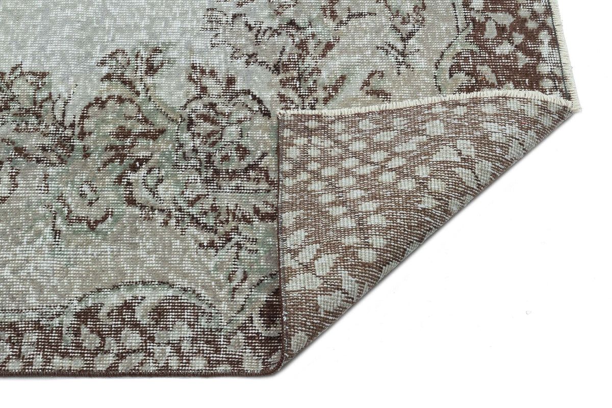 Grey and brown distressed floral medallion rug with a corner folded over to show the woven backing.
