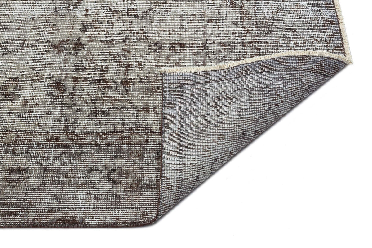 Distressed brown and cream traditional rug with a folded corner revealing the woven backing and fringe edge.