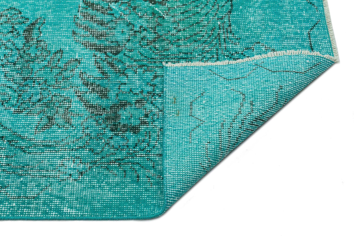Teal rug with a black floral medallion pattern and a folded corner showing the woven backing on a white background.