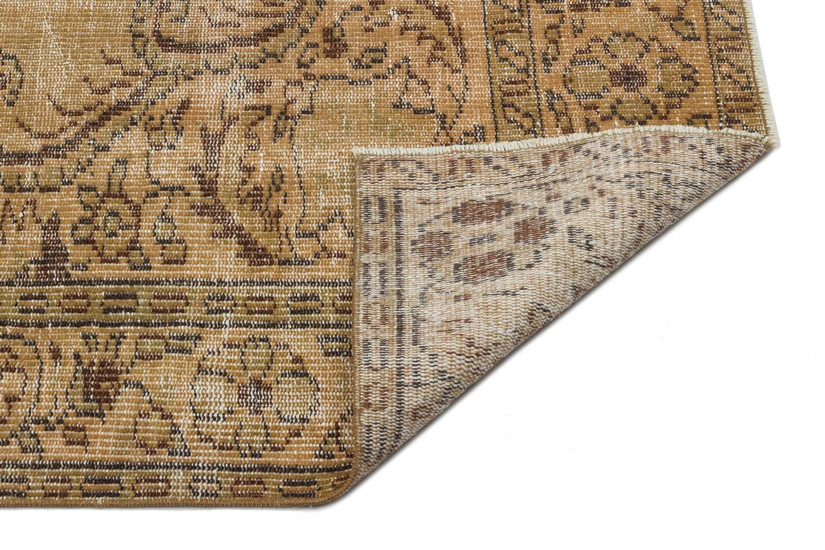 Tan and brown distressed rug with a traditional floral medallion pattern, showing a folded corner on a white background.