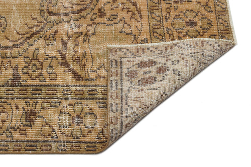 Load image 1 in gallery view. Tan and brown distressed rug with a traditional floral medallion pattern, showing a folded corner on a white background.
