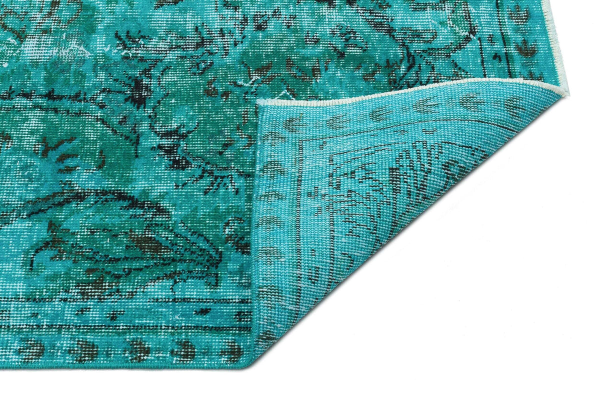 Turquoise and black distressed medallion rug with a folded corner showing the woven backing.