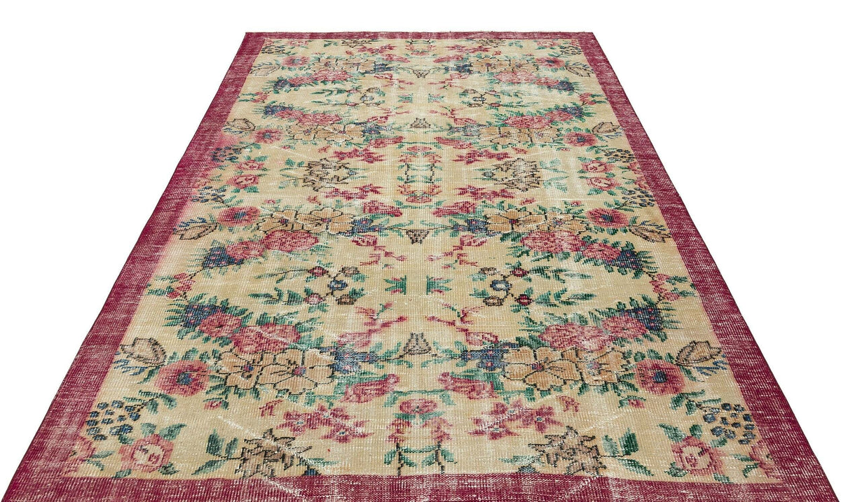 Beige vintage-style rug with a distressed floral pattern in red, blue, and green, featuring a wide red border.