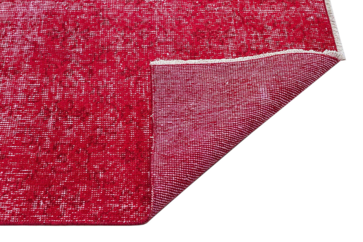 Distressed red rug with a white speckled pattern, shown with a corner folded back to reveal the woven underside.