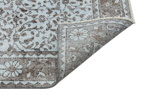 Load image 1 in gallery view. Light blue and brown rug with a traditional floral medallion pattern, shown with a corner folded over on white.