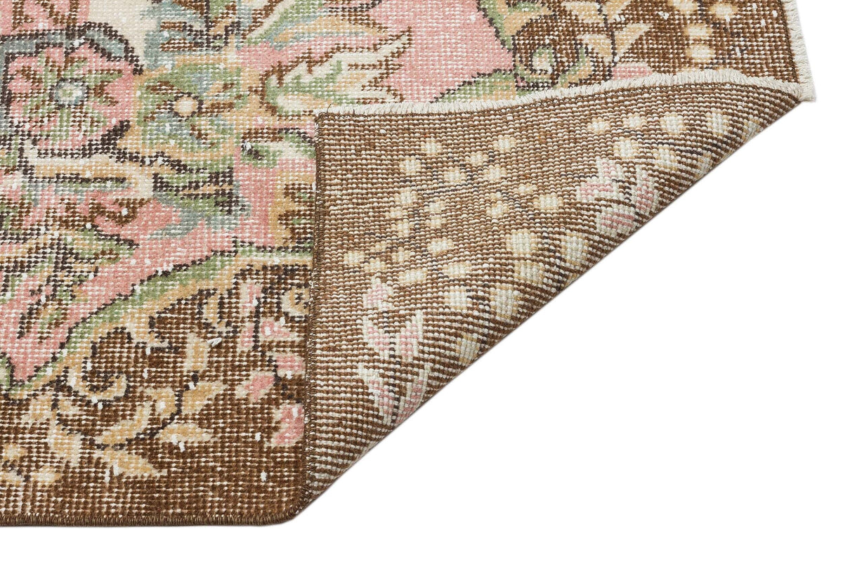 Distressed floral medallion rug in pink, sage green, and brown, showing a folded corner on a white background.