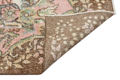 Load image 1 in gallery view. Distressed floral medallion rug in pink, sage green, and brown, showing a folded corner on a white background.