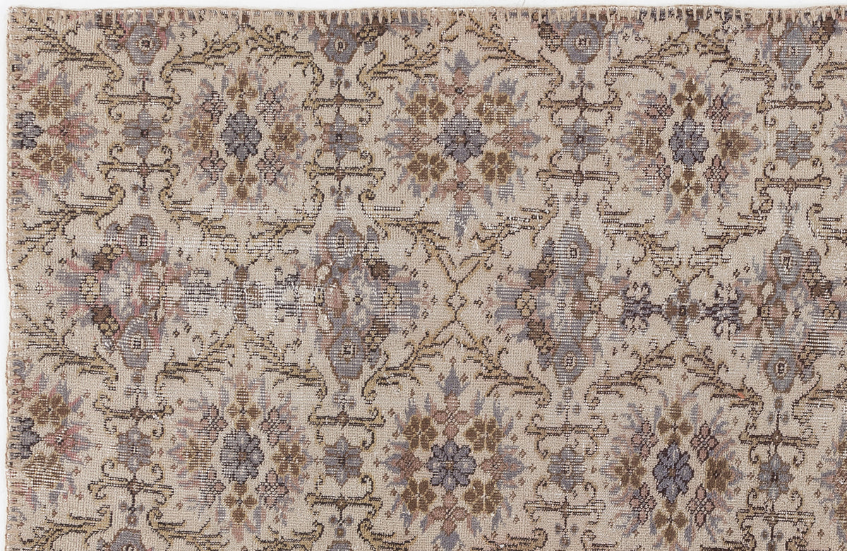 Beige rug with a distressed, repeating floral medallion pattern in muted tones of slate blue, brown, and soft pink.