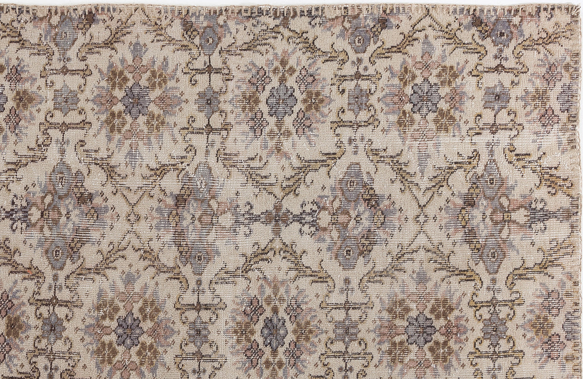 Beige rug with a distressed, repeating floral medallion pattern in muted brown, grey, and dusty rose tones.