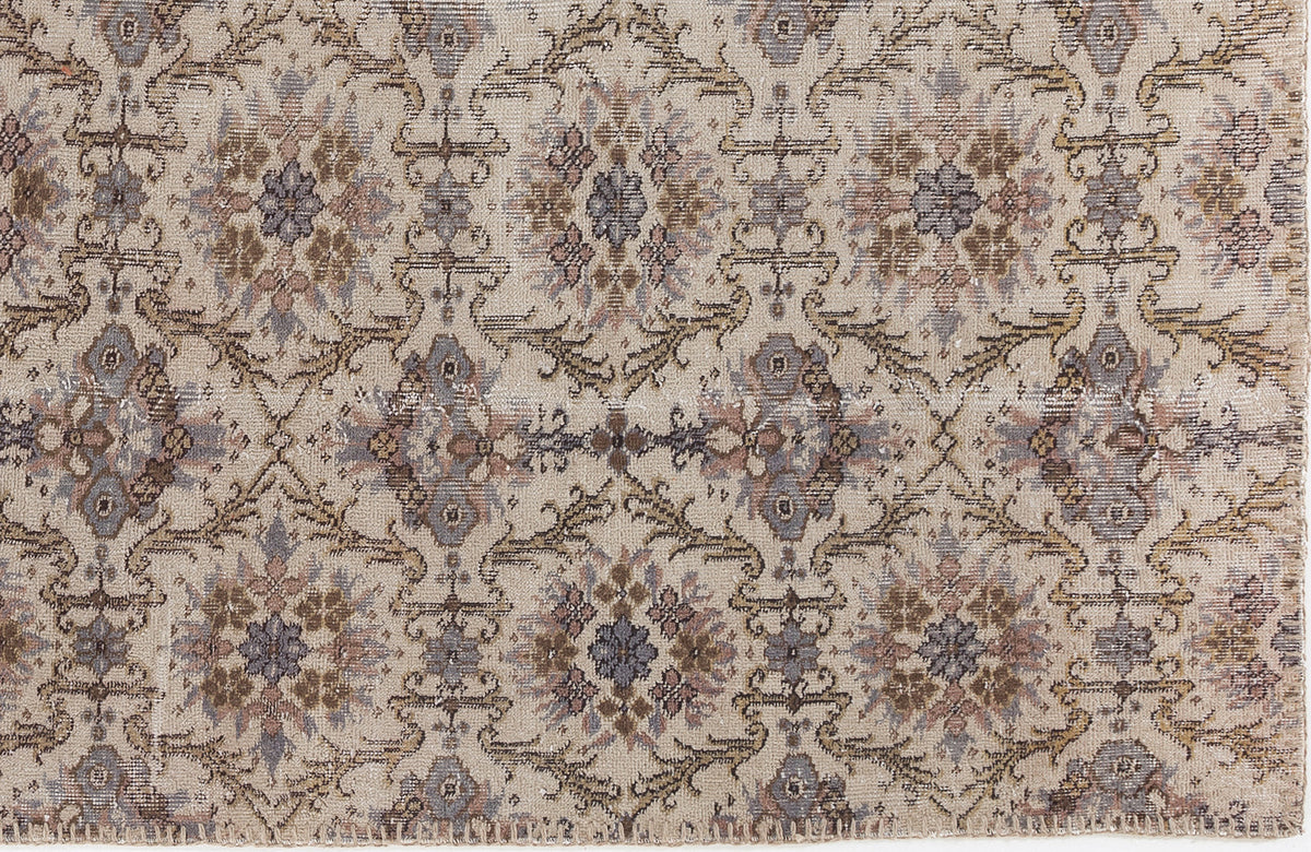 Beige rug with a distressed, repeating floral medallion pattern in muted tones of brown, grey, and mauve.