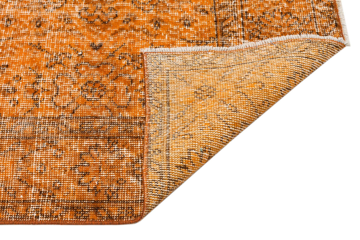 Burnt orange and brown distressed rug with a traditional floral medallion pattern, shown with a folded corner.