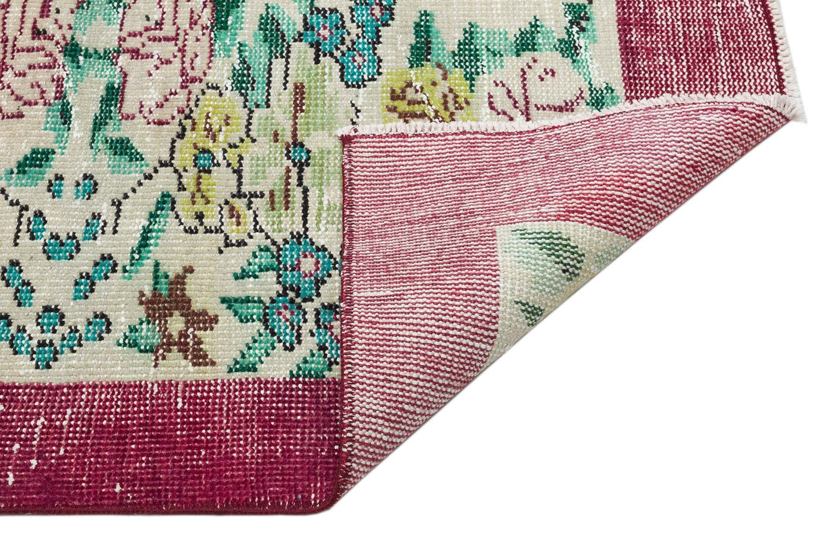 Cream rug with floral pattern in teal, yellow, and magenta, featuring a folded corner revealing the woven backing.