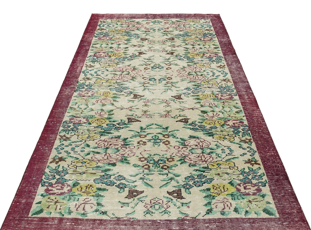 Beige runner rug with a distressed floral pattern in pink, yellow, and teal, featuring a wide burgundy border.