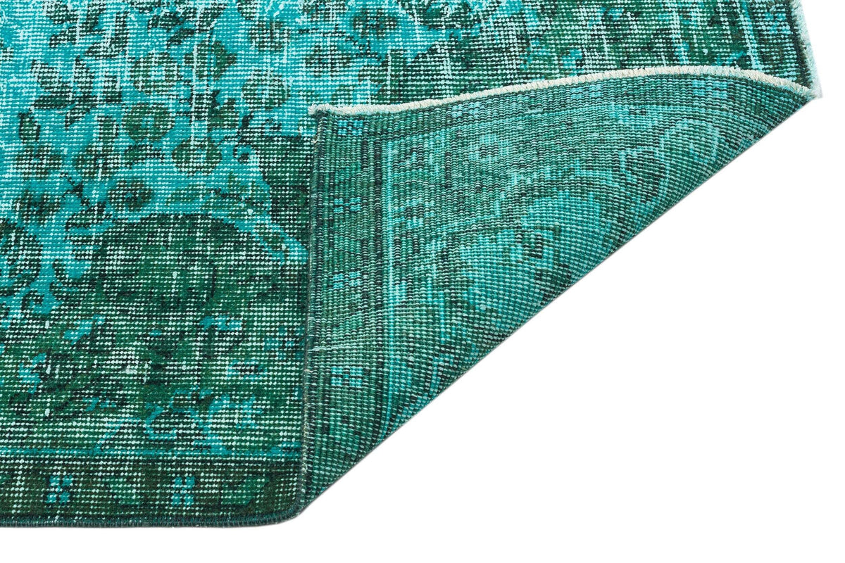 Teal and dark green distressed rug with a traditional medallion pattern, shown with a corner folded over.