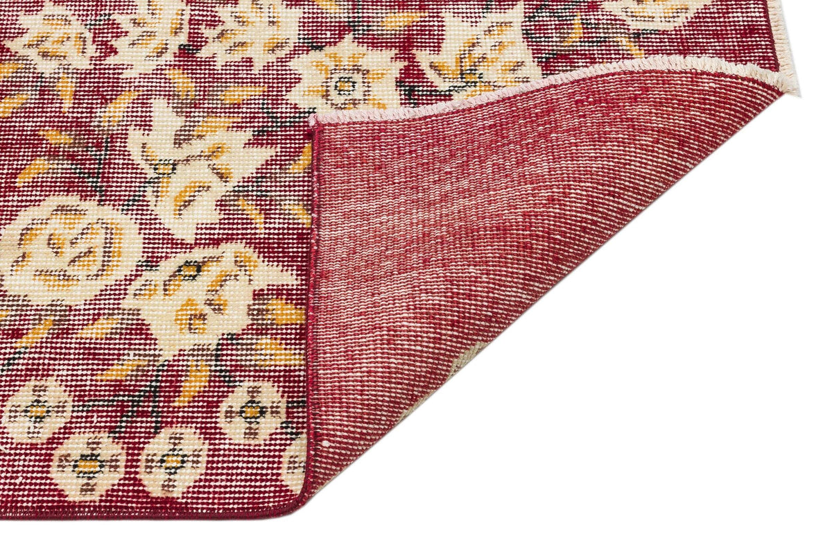 Deep red rug with cream and gold floral patterns, shown with a corner folded to reveal the woven backing.