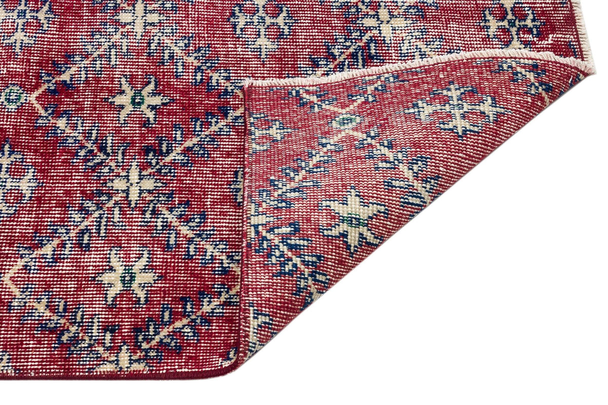 Red rug with a blue and cream floral geometric pattern, shown with a corner folded over to reveal the underside.