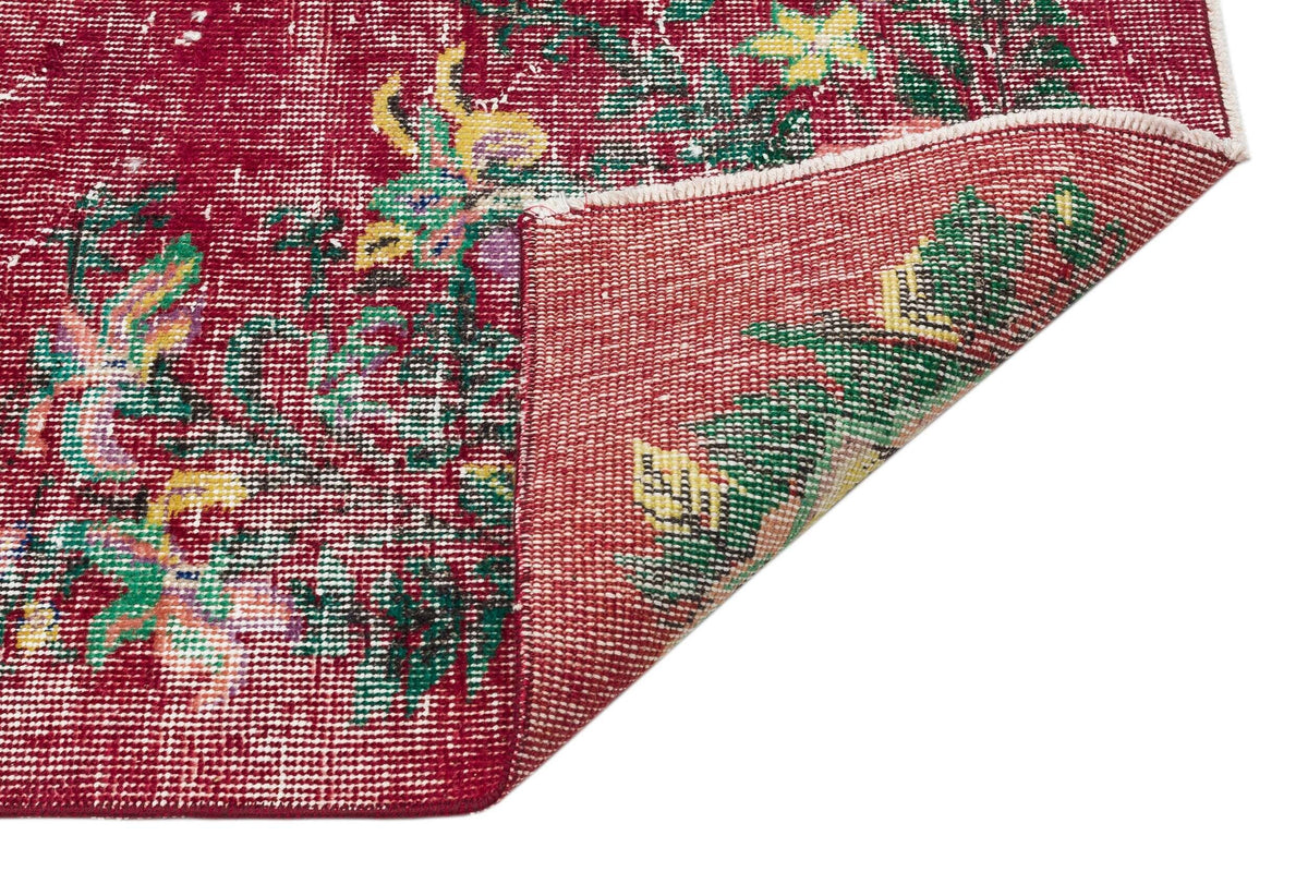 Distressed crimson rug with a floral pattern in green and yellow, shown with a corner folded over on a white background.