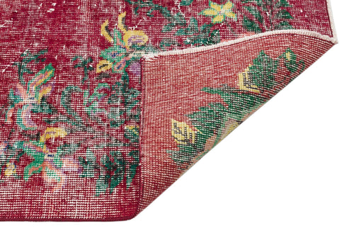 Load image 1 in gallery view. Distressed crimson rug with a floral pattern in green and yellow, shown with a corner folded over on a white background.