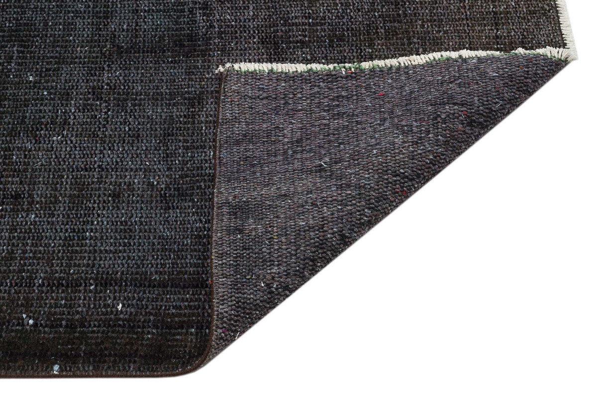 Charcoal grey rug with a textured, distressed finish and a folded corner revealing the dark woven backing.
