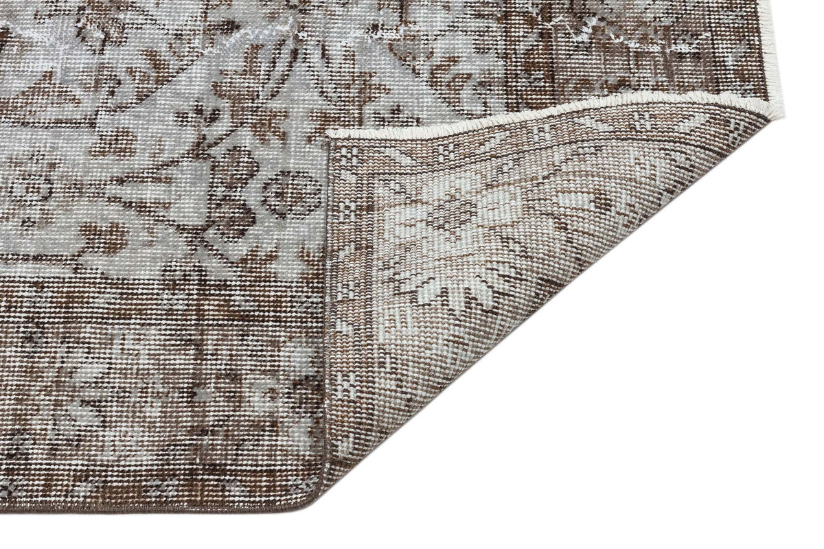 Brown and grey distressed traditional rug with a floral medallion pattern, shown with a corner folded over.