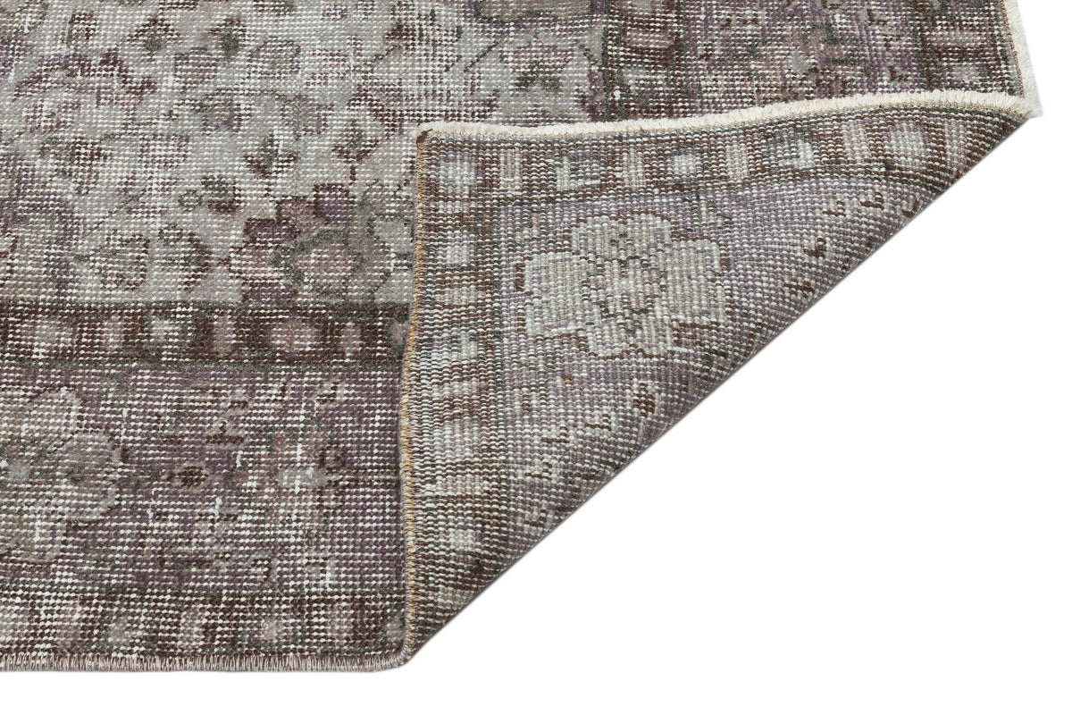 Grey and brown distressed traditional rug with a floral medallion pattern, shown with a folded corner on white.