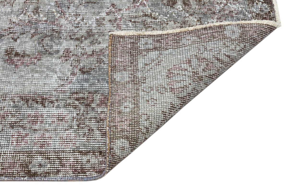Grey and brown distressed traditional rug with a floral medallion pattern, shown with a corner folded over.