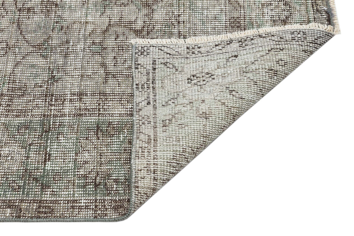 Distressed sage green and brown traditional medallion rug with a folded corner showing the woven backing.