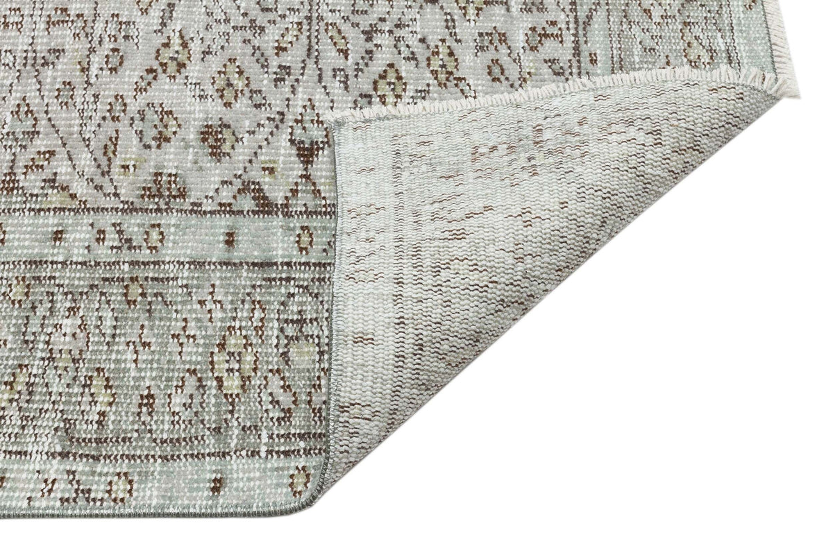 Light gray and brown distressed traditional rug with a floral pattern, shown with a folded corner revealing the backing.