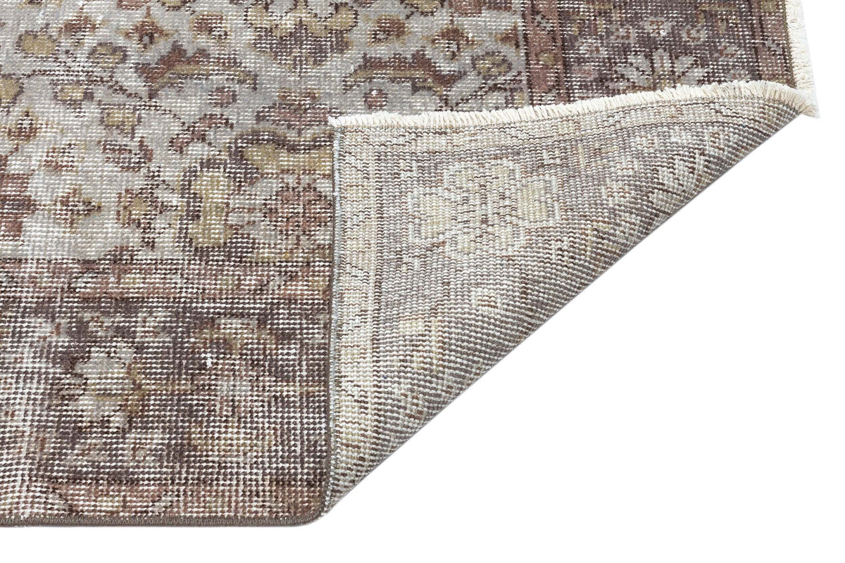 Distressed brown and beige traditional rug with a floral medallion pattern, shown with a corner folded to reveal the backing.