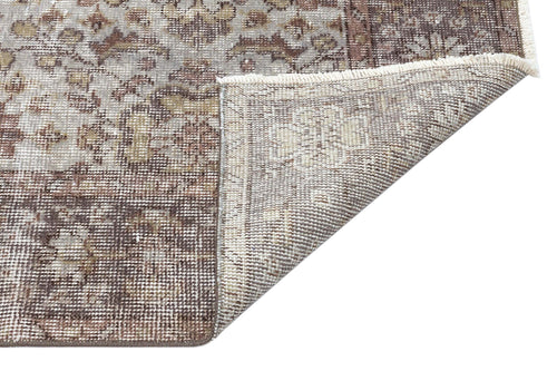Load image 1 in gallery view. Distressed brown and beige traditional rug with a floral medallion pattern, shown with a corner folded to reveal the backing.