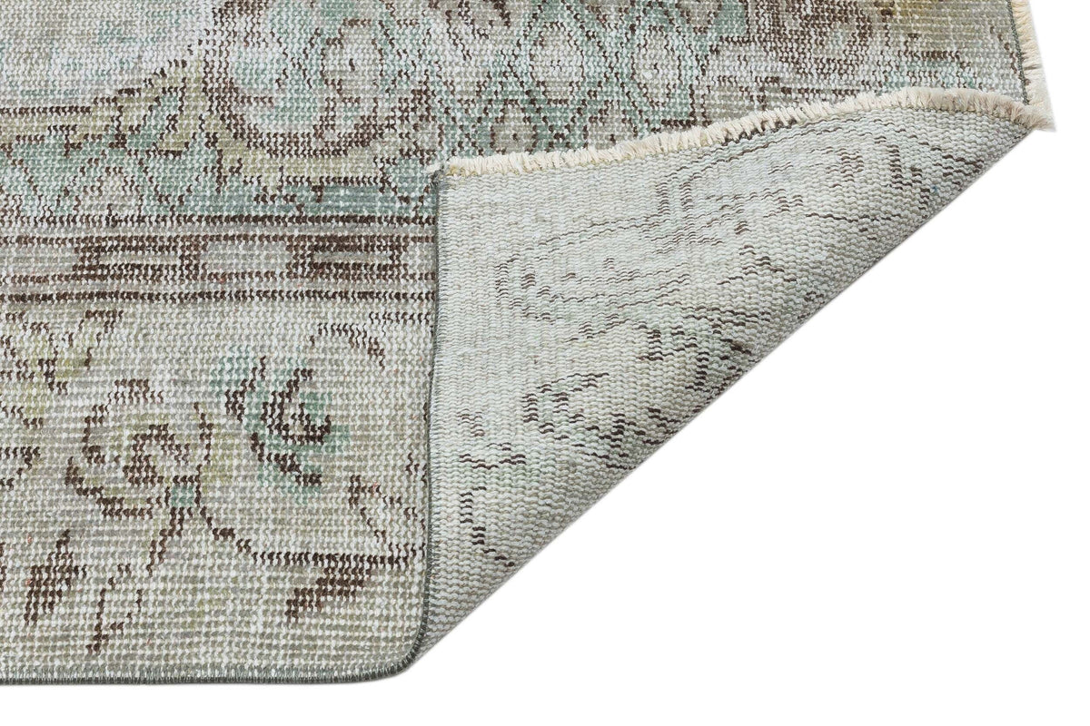 Distressed sage green and brown traditional medallion rug with a folded corner showing the woven backing.